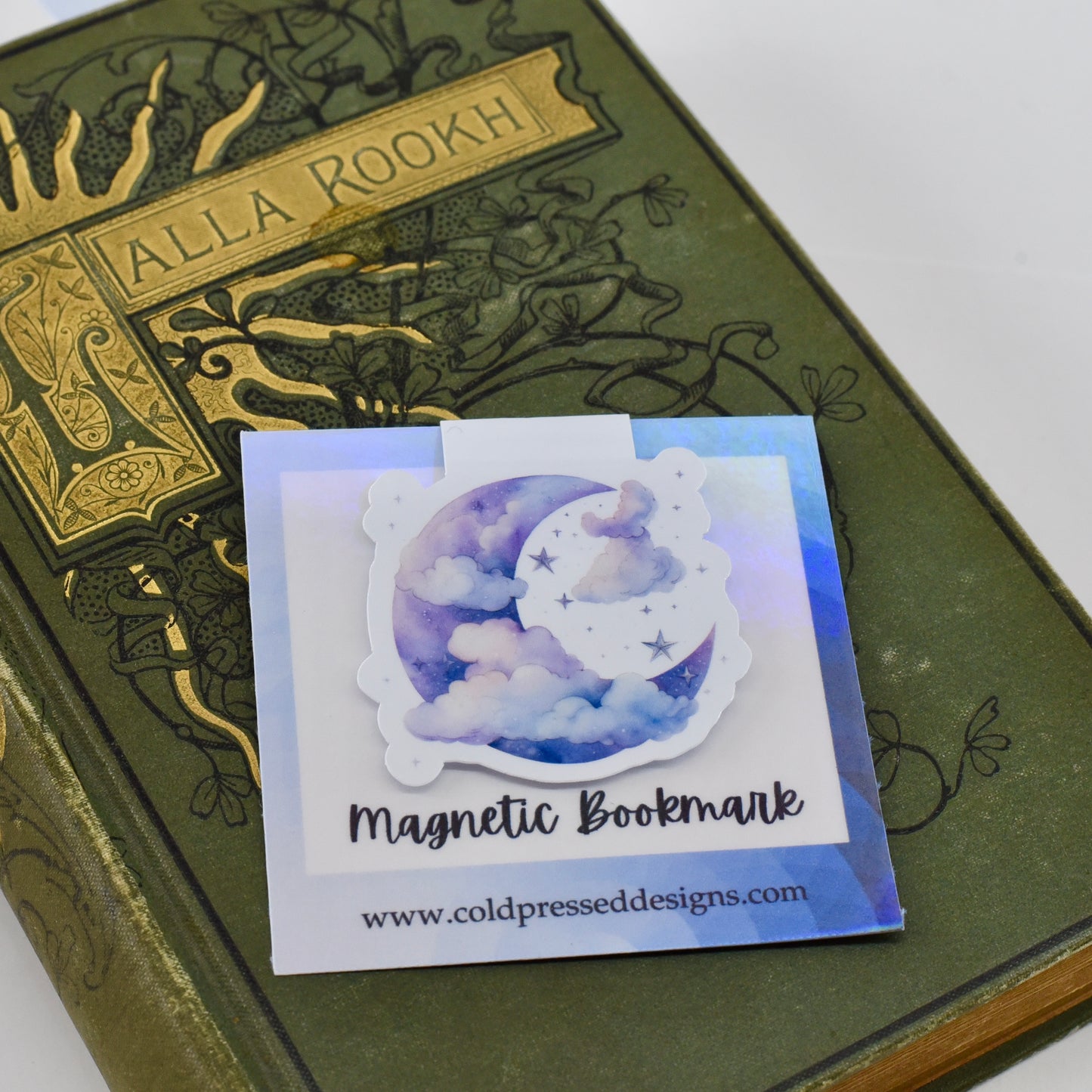 A closed glossy magnetic bookmark with a design of a blue moon and clouds on it.