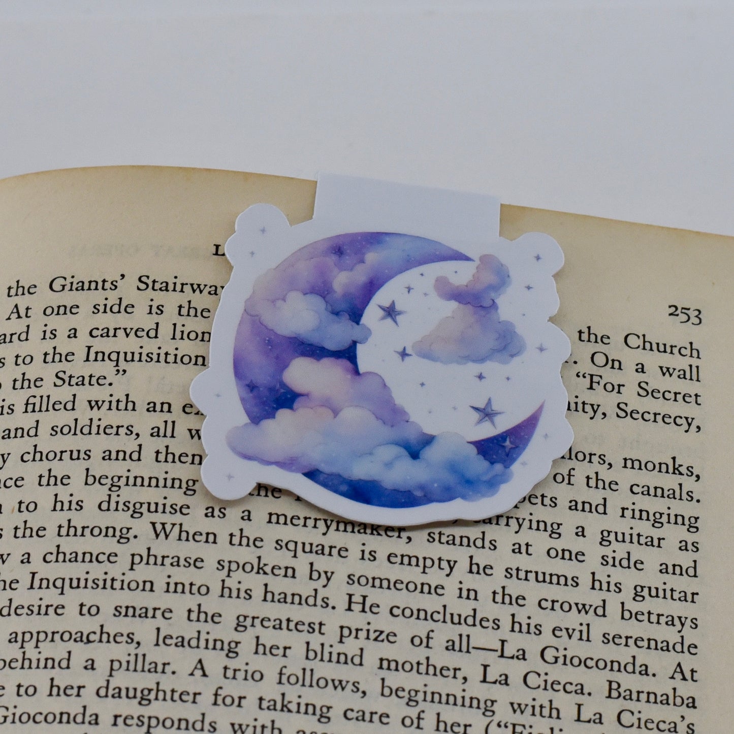 A closed glossy magnetic bookmark with a design of a blue moon and clouds on it.
