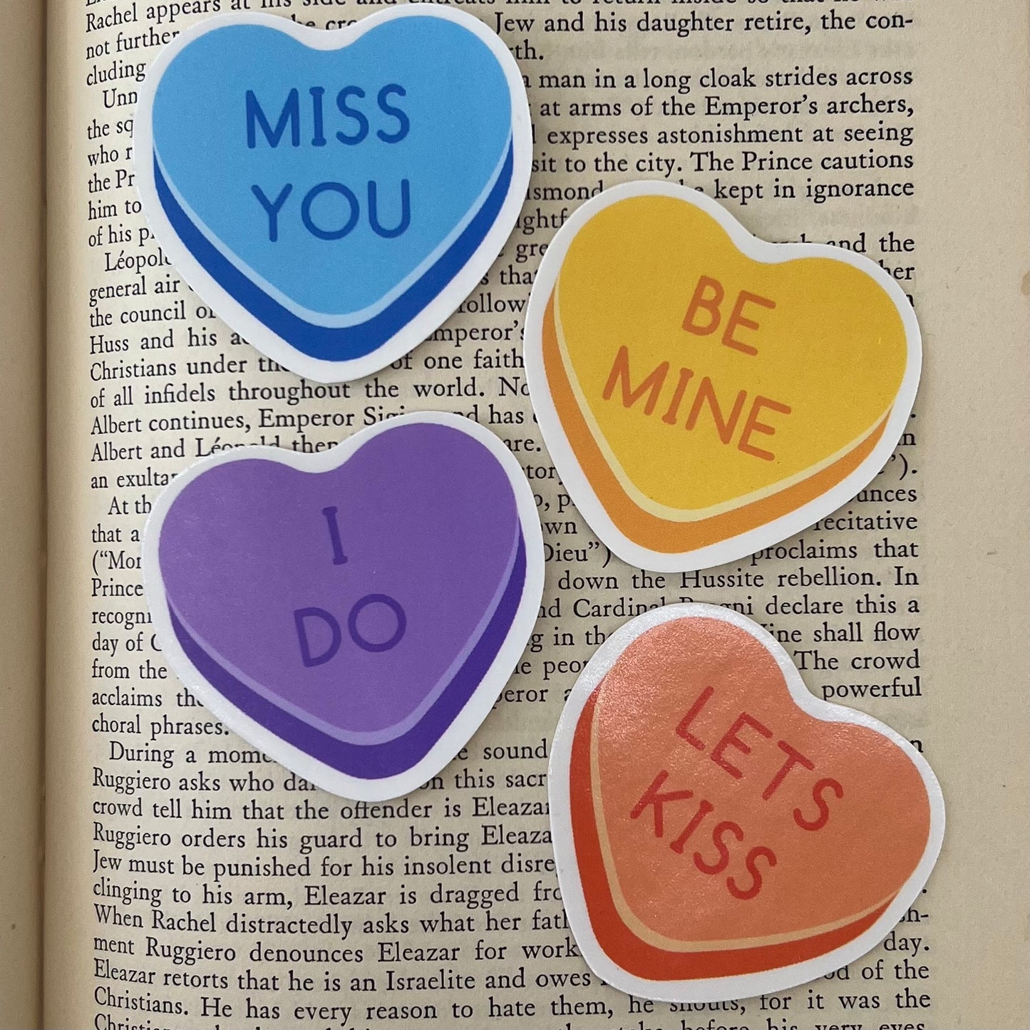 A set of four vinyl stickers with heart-shaped designs and various affectionate phrases written on them, placed on a book page.