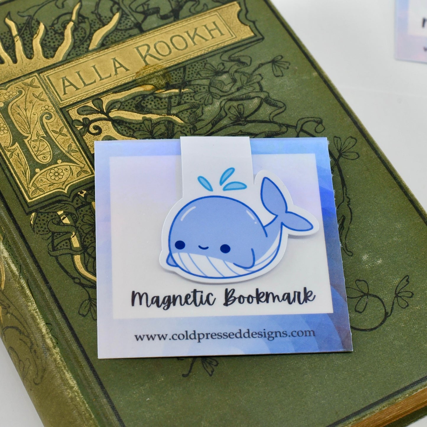 A handmade magnetic bookmark in a whale design with a happy kawaii face, featuring a glossy finish and a magnetic closure.