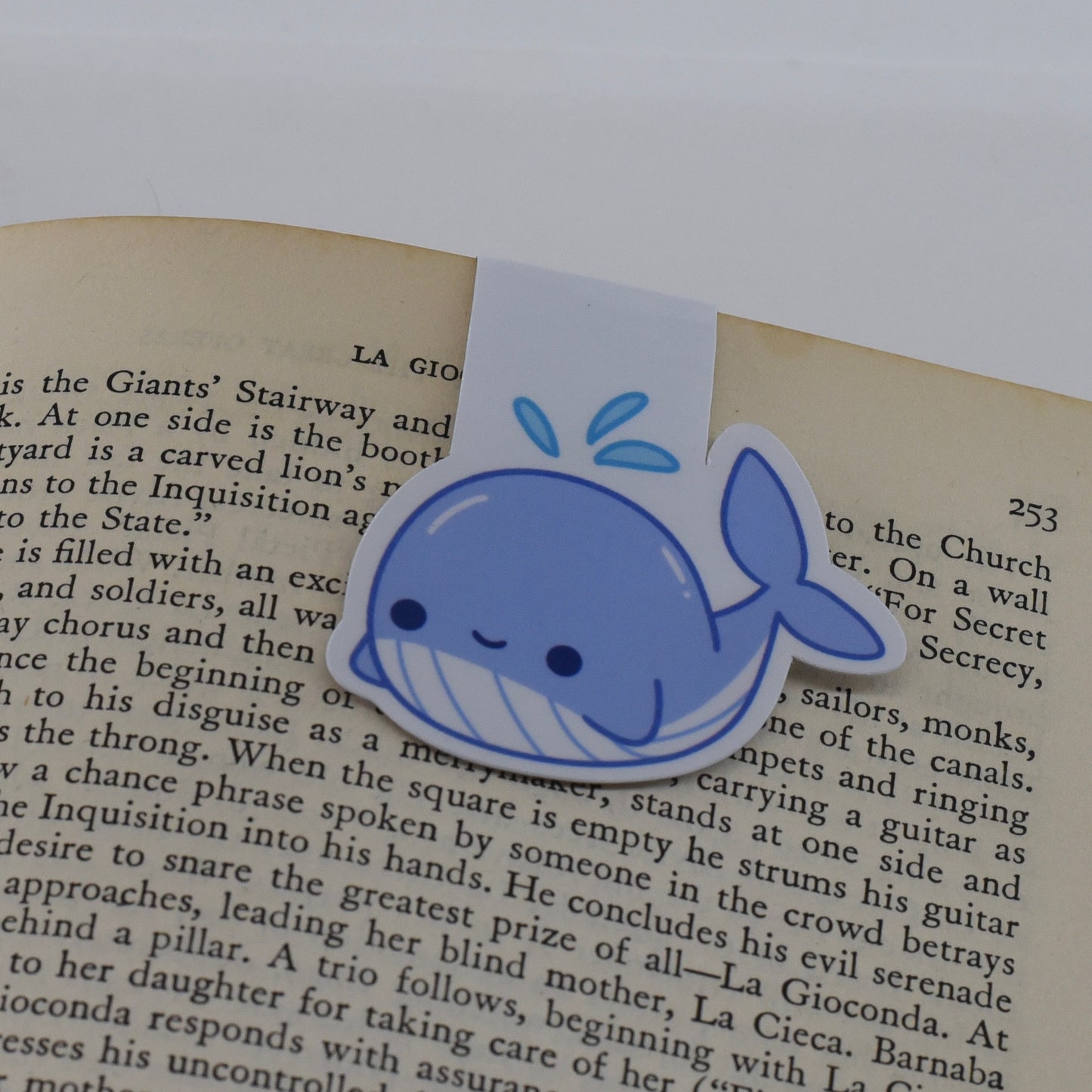 A handmade magnetic bookmark in a whale design with a happy kawaii face, featuring a glossy finish and a magnetic closure.