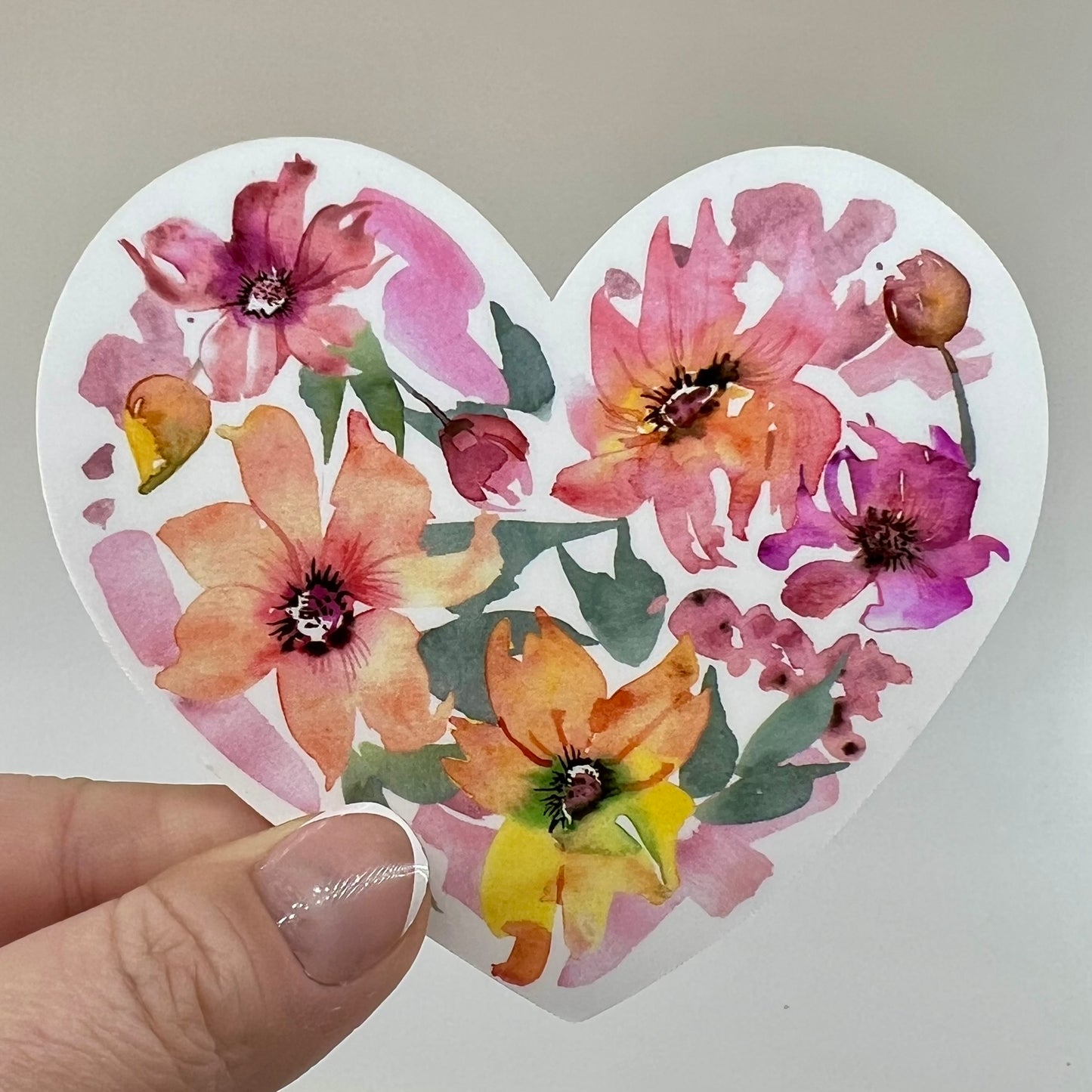A vinyl sticker with a pink and orange watercolor floral design in a heart shape.