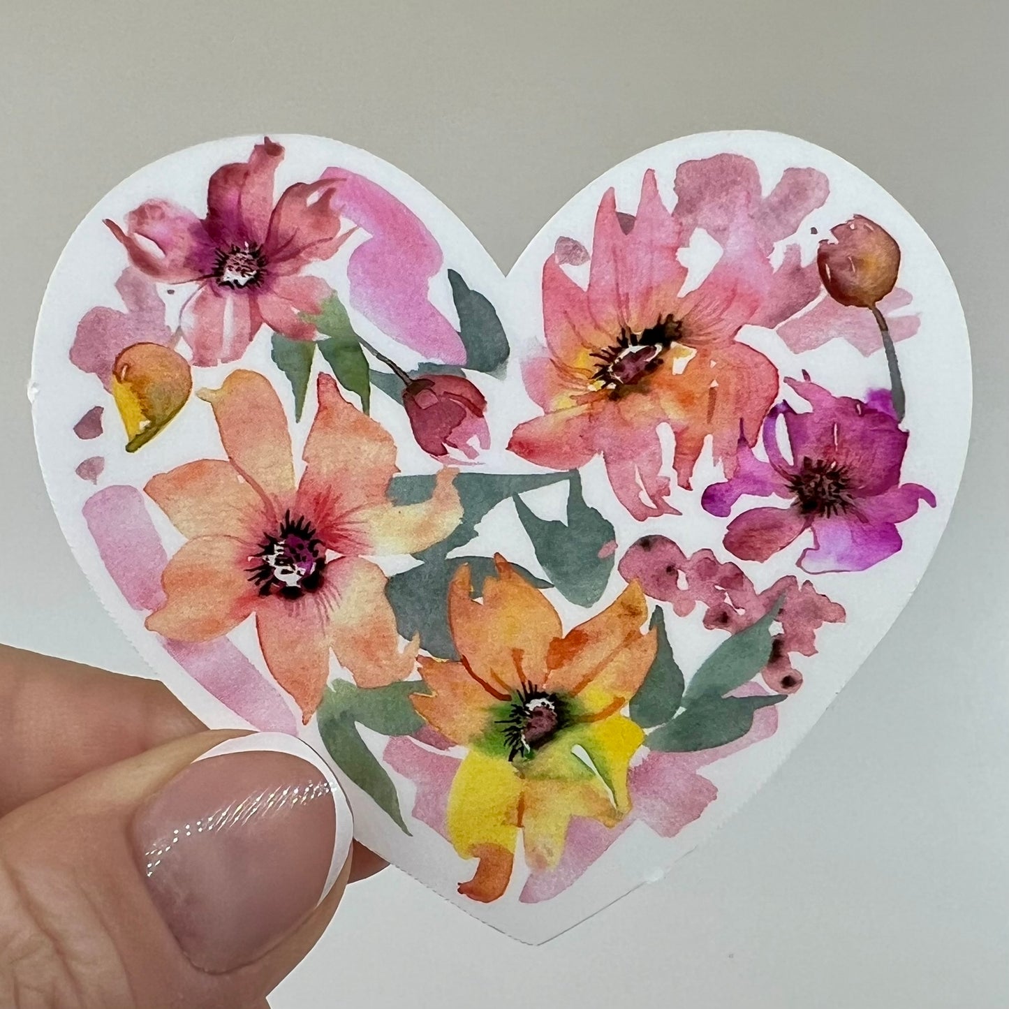 A vinyl sticker with a pink and orange watercolor floral design in a heart shape.