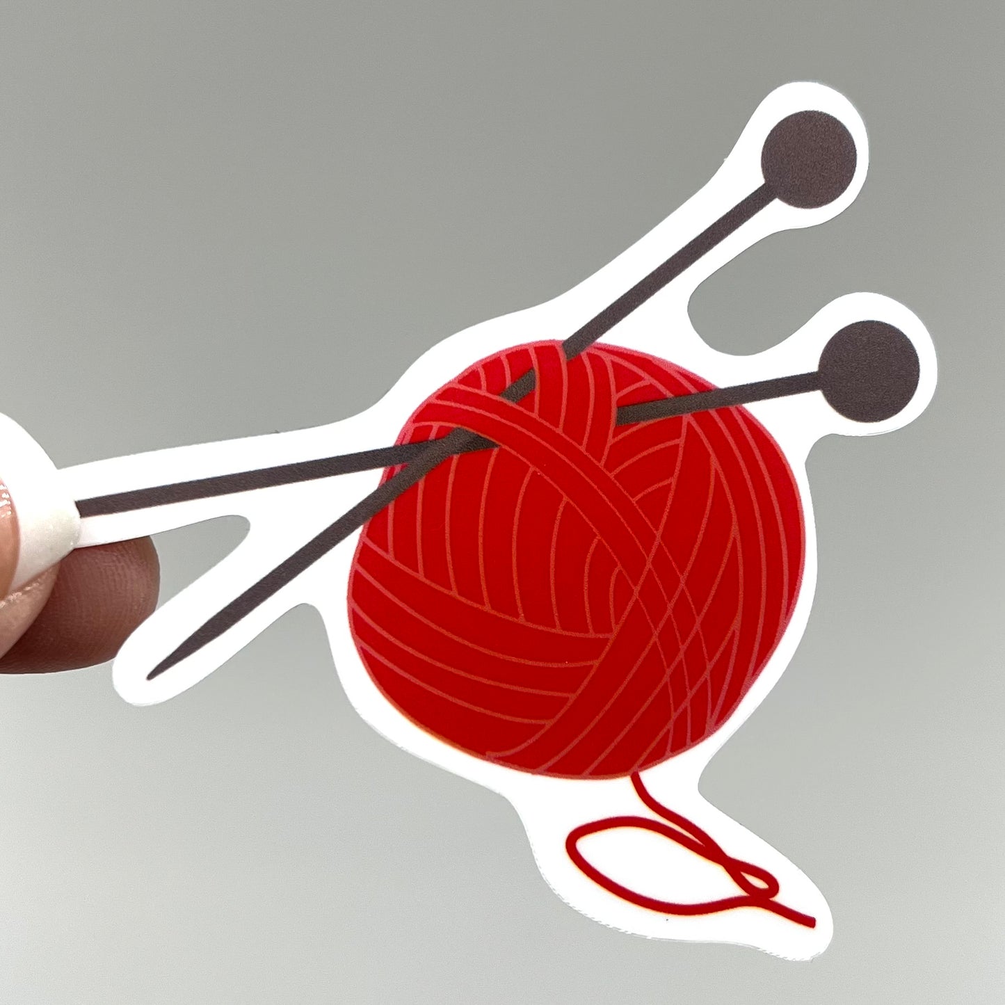 A vinyl sticker depicting a red ball of yarn with knitting needles.