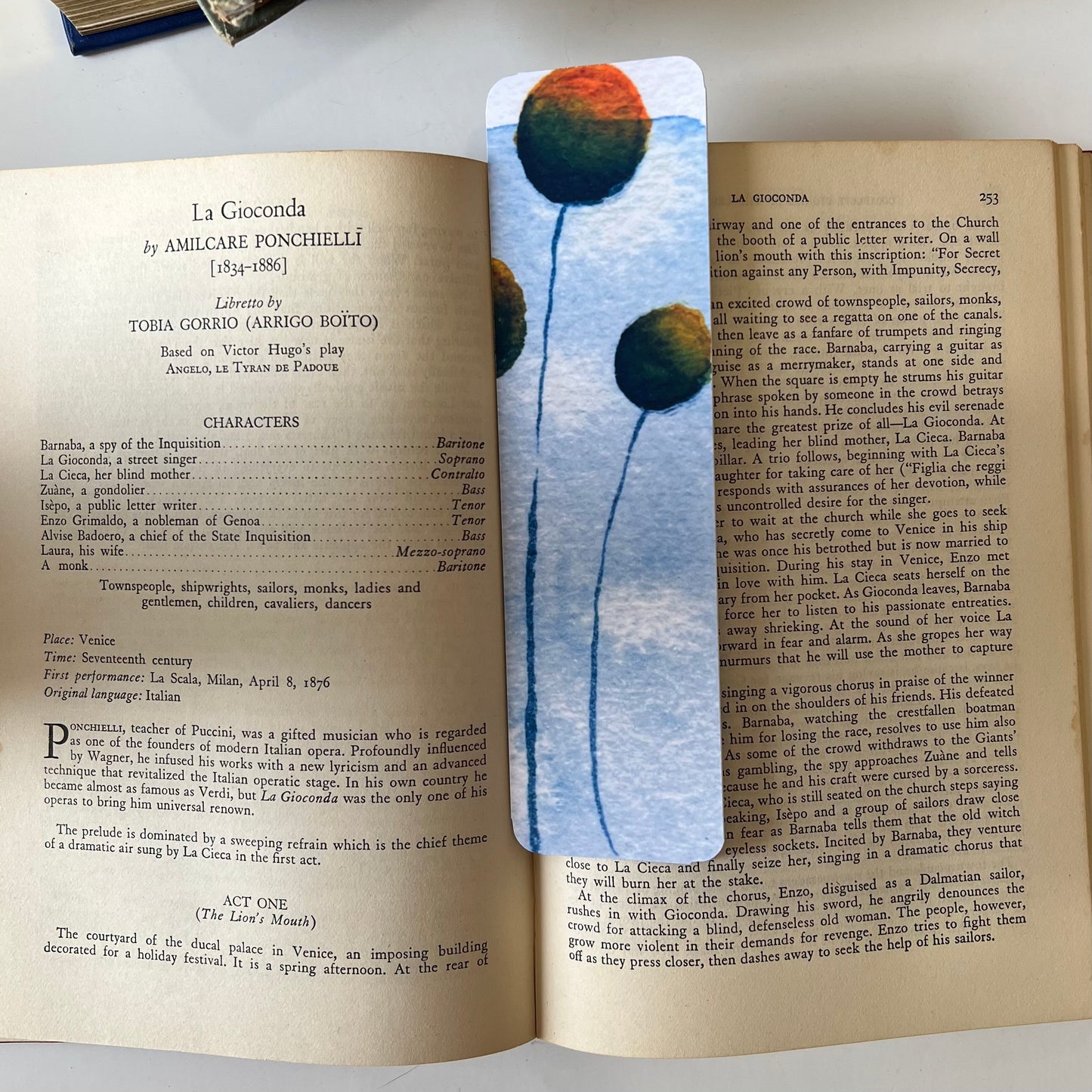 A glossy handmade bookmark with a watercolor floral doodle in blue, green and orange.