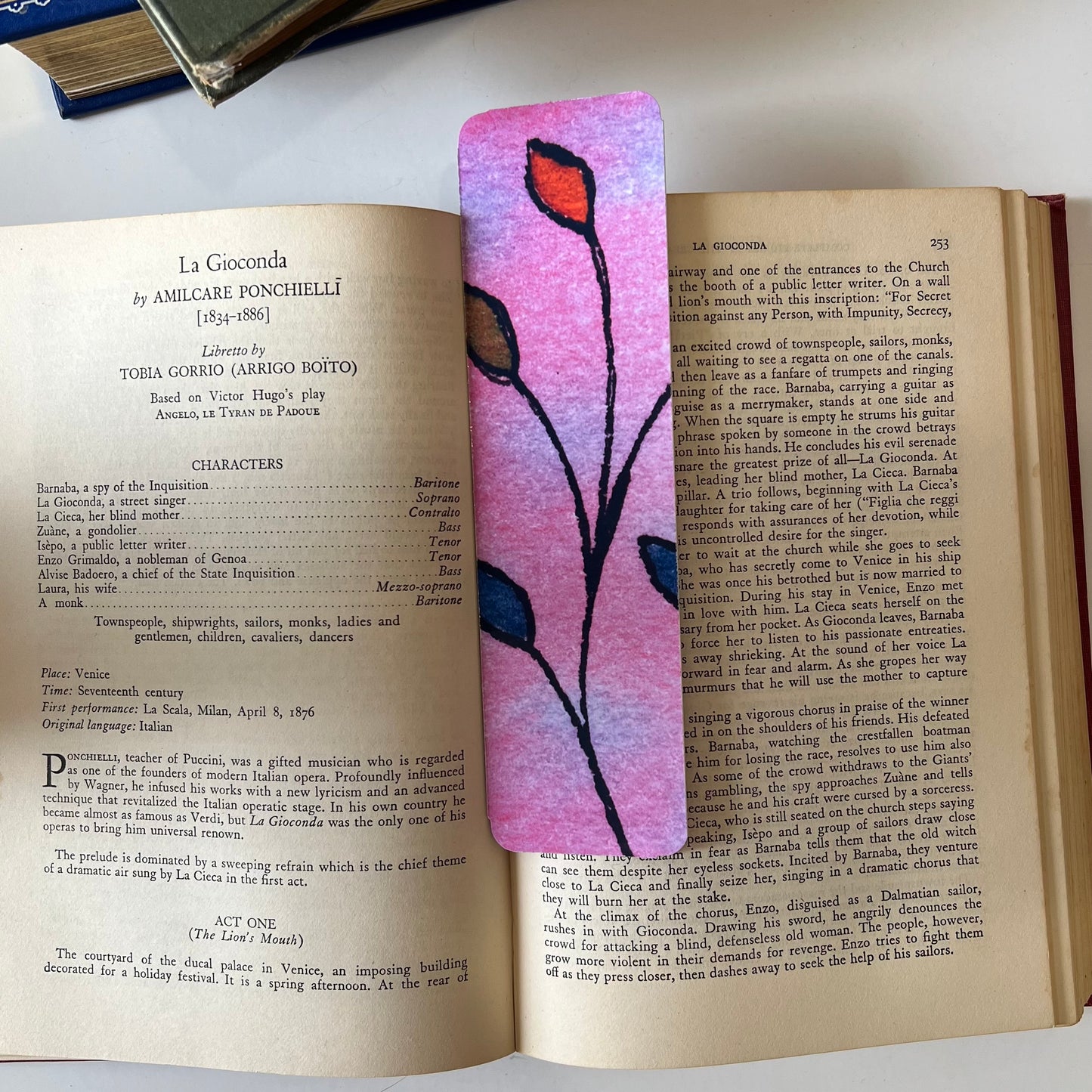 A glossy handmade bookmark with a watercolor floral doodle in pink, orange and blue.