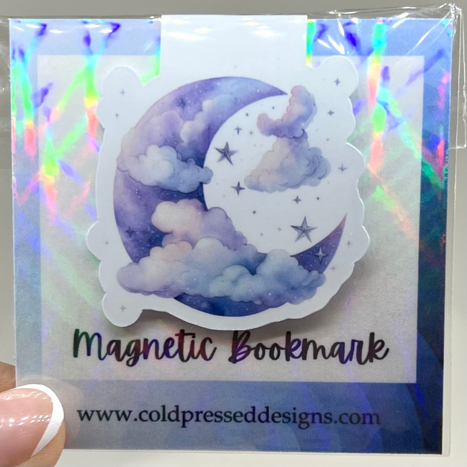 A closed glossy magnetic bookmark with a design of a blue moon and clouds on it.