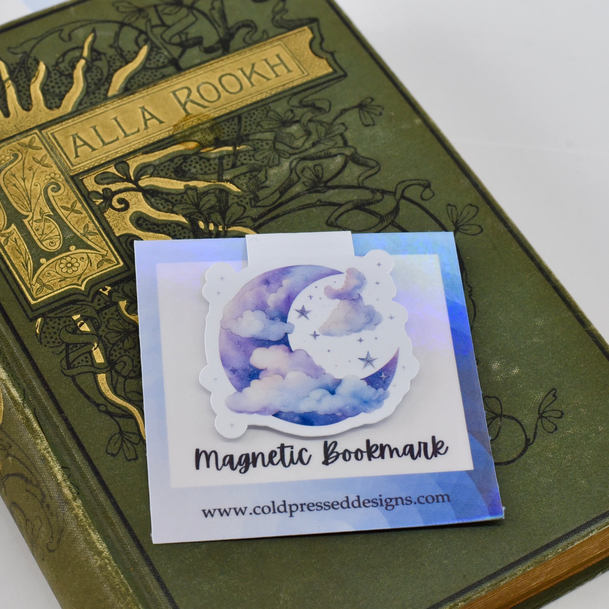 A closed glossy magnetic bookmark with a design of a blue moon and clouds on it.
