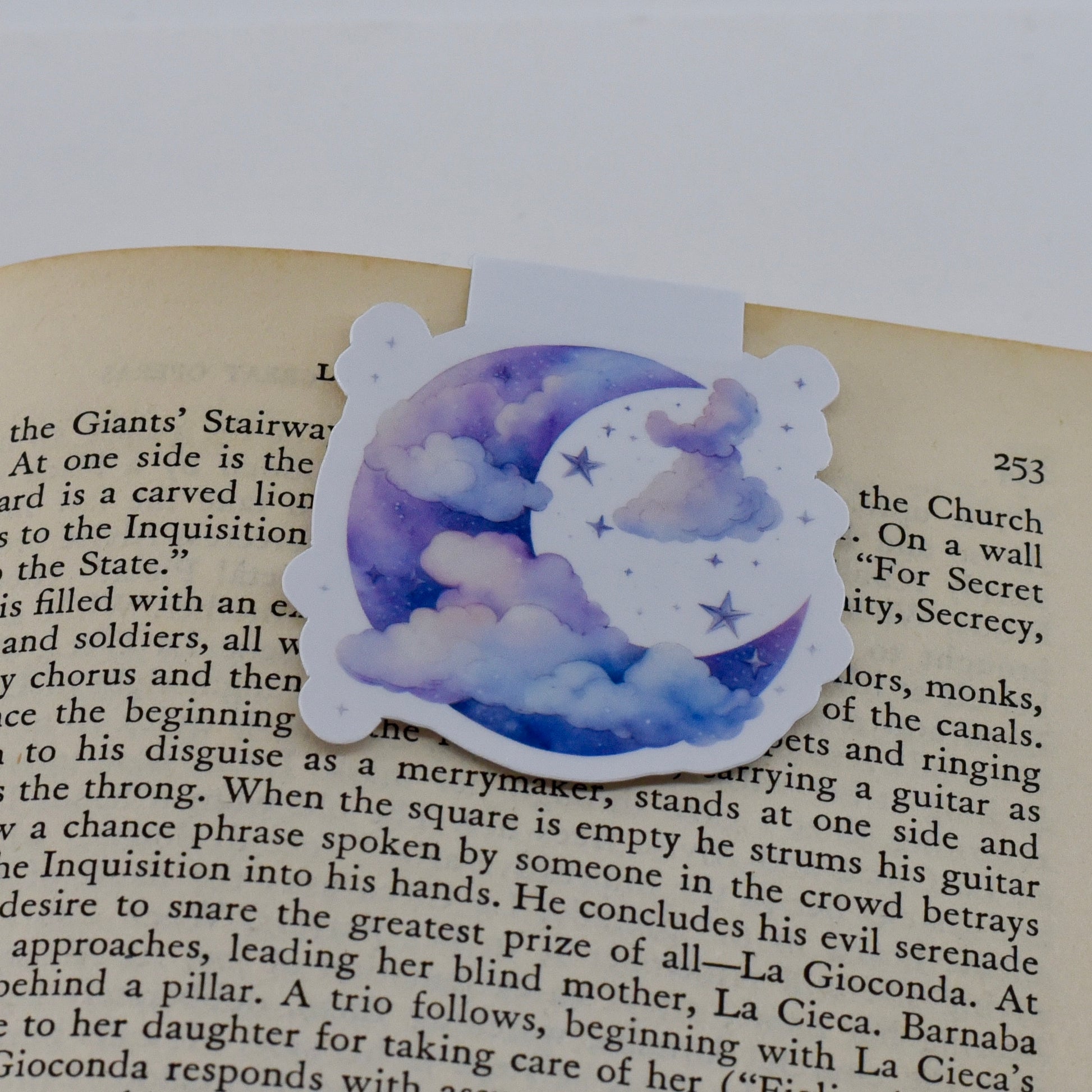 A closed glossy magnetic bookmark with a design of a blue moon and clouds on it.