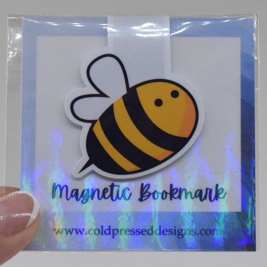 A handmade magnetic bookmark with a bumble bee design, displayed in a packaging with the text 'Magnetic Bookmark' and the brand name 'Cold Pressed Designs'. The bookmark is visible through a clear plastic front.