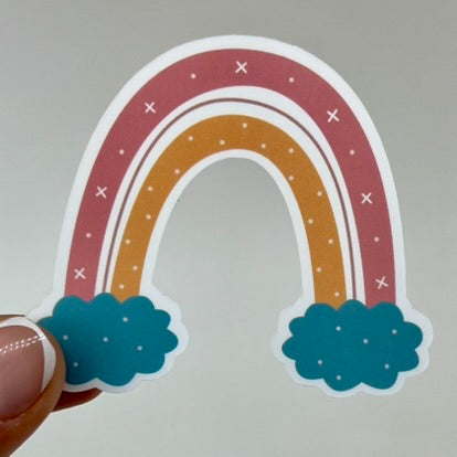 A vinyl sticker of a pink and orange rainbow stretching between two blue clouds.