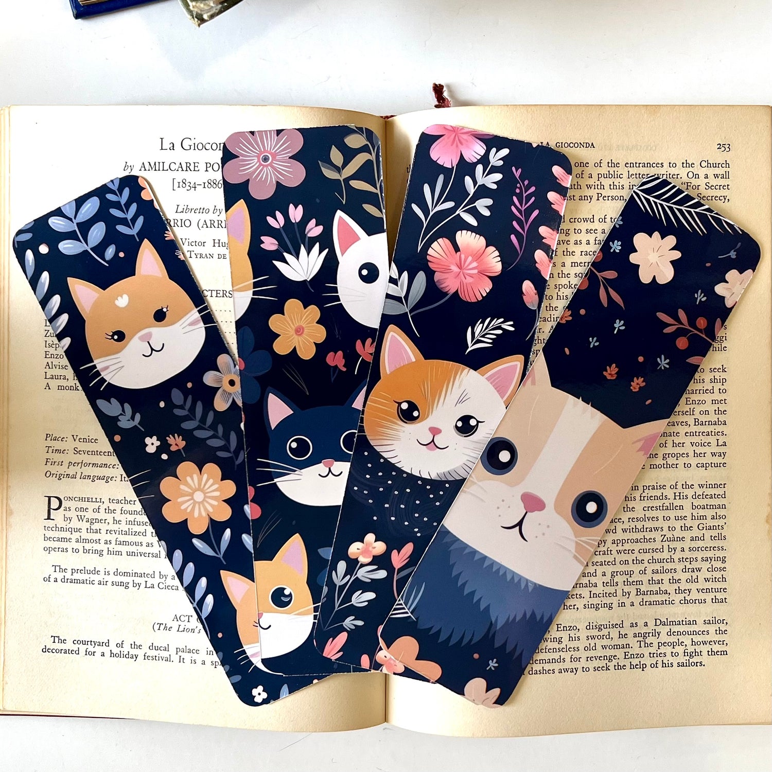 A set of handmade rectangular glossy bookmarks with cute cat faces and floral patterns on a navy background.