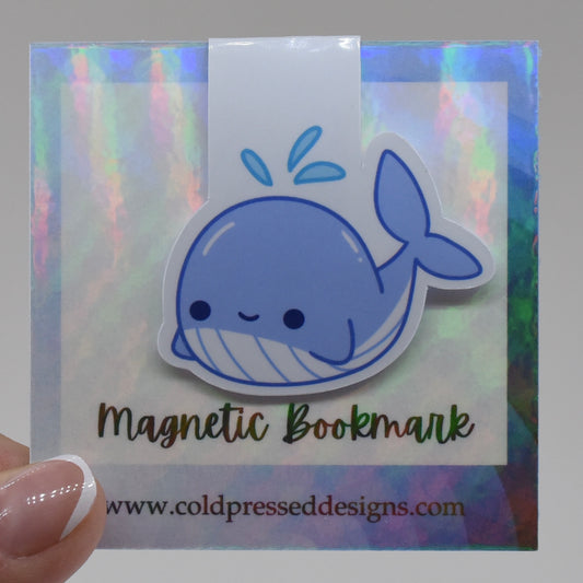 A handmade magnetic bookmark in a whale design with a happy kawaii face, featuring a glossy finish and a magnetic closure.
