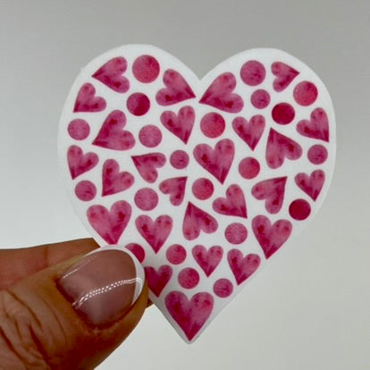 A white vinyl sticker in the shape of a heart with smaller pink hearts and pink circles inside which follow the shape of the heart.