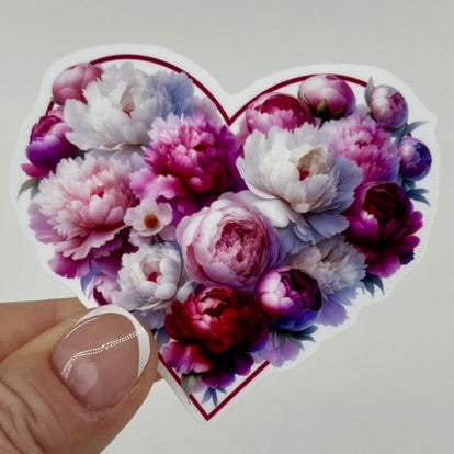 Fingers holding a heart sticker made of pink peonies.