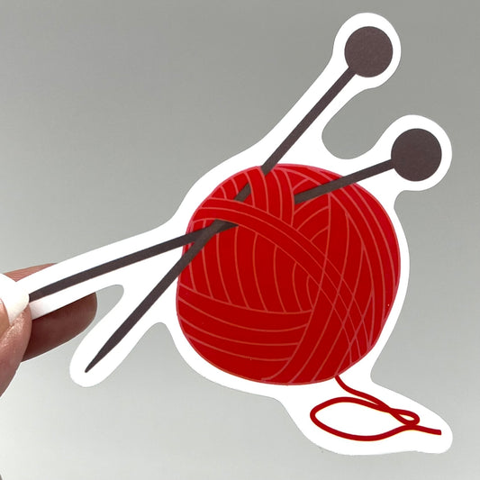 A vinyl sticker depicting a red ball of yarn with knitting needles.