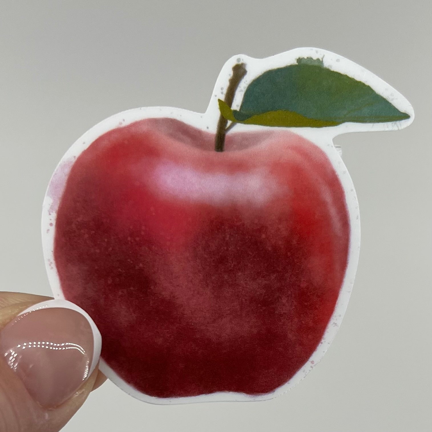 A vinyl sticker of a red watercolor apple with a stem and green leaf attached.