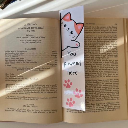 A rectangular bookmark with a cartoon cat face, the phrase 'YOU PAWSED HERE' and pink paw prints on a book.